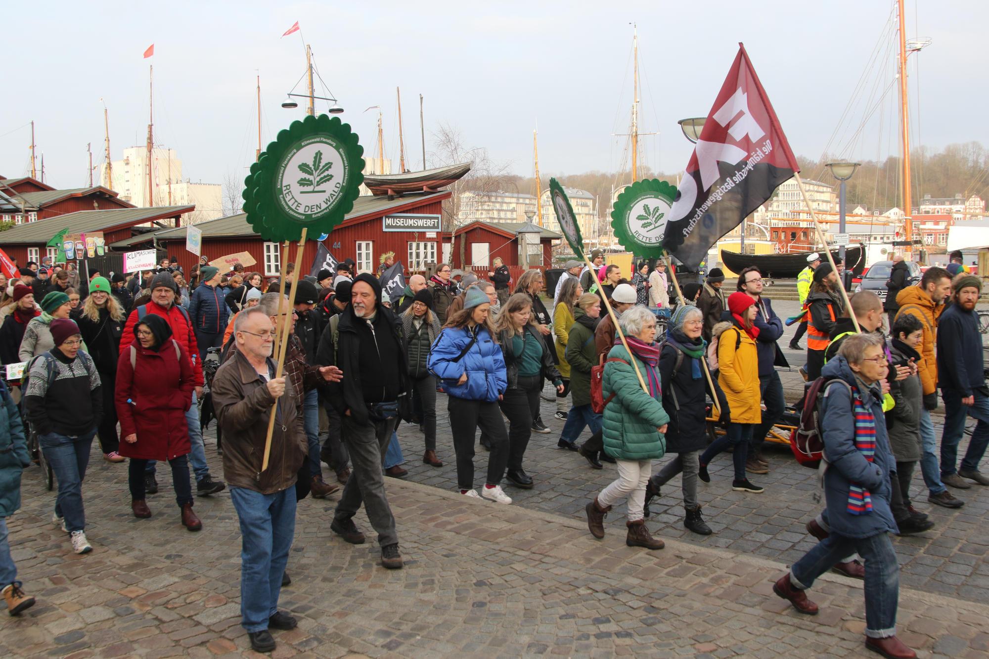 Klima-Demozug in Flensburg auf der Schiffbrücke. Menschen halten Fahnen und Plakate hoch.